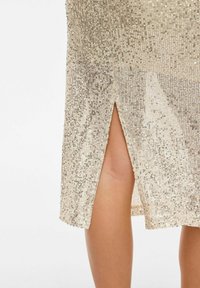 Beige paljettklänning med en sidosprund, med en texturerad yta av glittrande paljetter och en figurnära siluett.