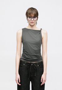 Haut gris sans manches en tissu lisse et extensible, avec des fronces sur le côté et un large décolleté. Associé à un jean foncé.