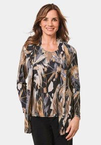 Langärmliges, leichtes Oberteil in abstrakten Schwarz-, Beige- und Grautönen, mit lockerer Passform und offenes Vorderdesign. Darunter werden schwarze Hose getragen.