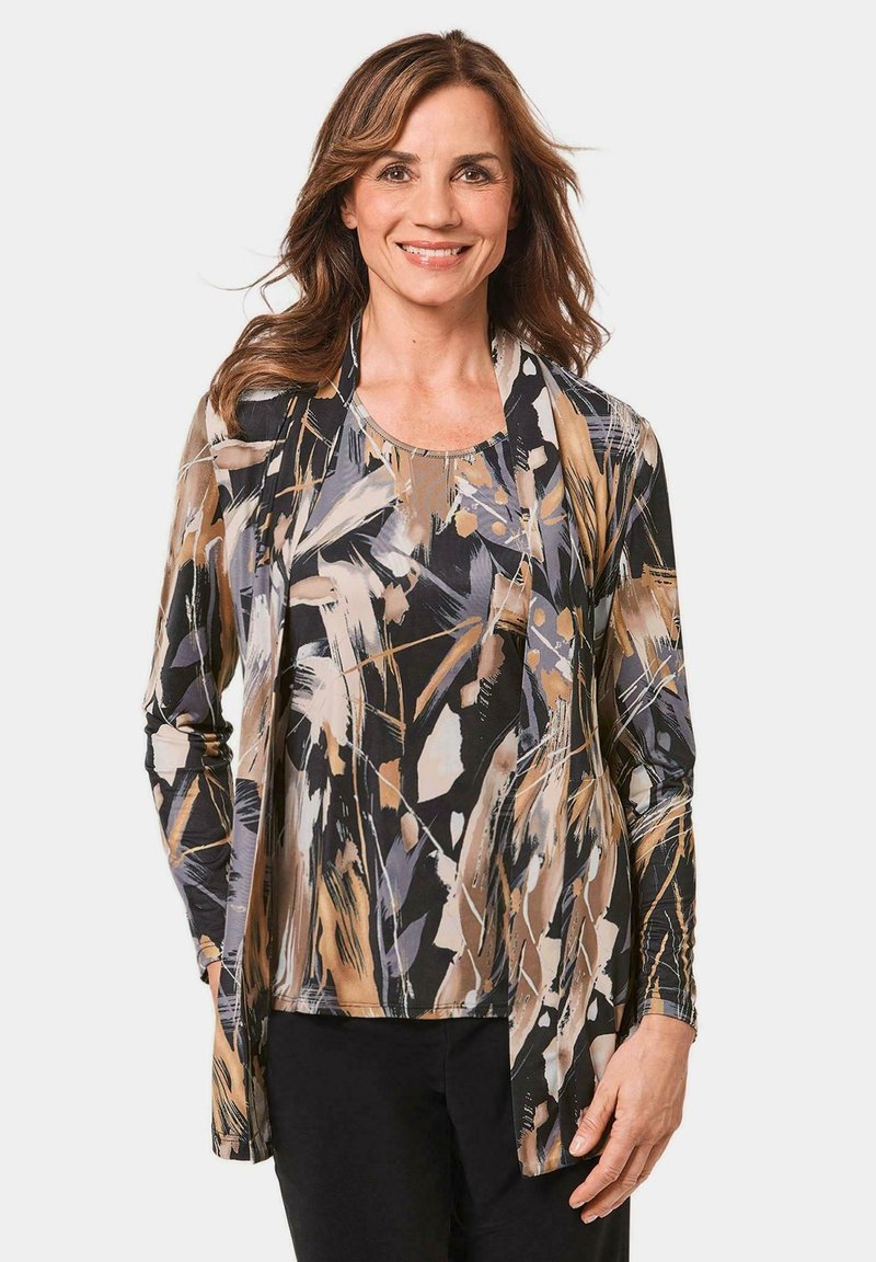 Langärmliges, leichtes Oberteil in abstrakten Schwarz-, Beige- und Grautönen, mit lockerer Passform und offenes Vorderdesign. Darunter werden schwarze Hose getragen.