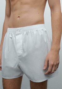 Bílé kraťasy s elastickým pasem, bočními kapsami a hladkým, lehkým materiálem. Délka ke kolenům a bez ozdob.