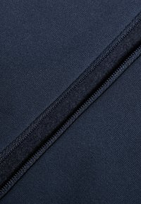 Tessuto blu navy con una texture liscia, caratterizzato da una cerniera nascosta e una cucitura accentuata che scorre verticalmente lungo il centro.