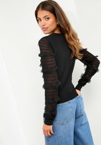 Schwarzer Pullover mit durchsichtigen, gerafften Mesh-Ärmeln mit einem strukturierten Muster; enganliegende Bündchen und Taillenbund im klassischen Design.