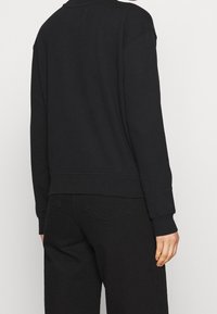Sudadera negra de corte relajado, con puños y dobladillo acanalados. La tela parece suave con una textura lisa; sin patrones ni adornos visibles.