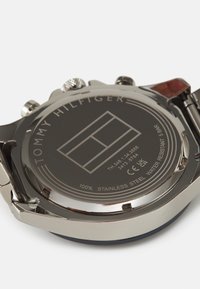 Fondo de reloj de acero inoxidable con logotipo de marca y detalles grabados. Presenta una textura metálica, forma redonda y marcas de resistencia al agua.