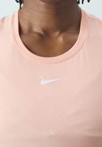 Gros plan d'une personne portant un haut Nike rose clair avec un logo swoosh blanc centré sous le col.