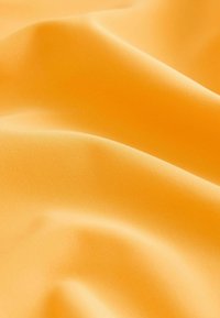 Spilgti oranža auduma ar gludu, matētu faktūru, kas izceļas ar mīkstiem drapējumiem un smalkām krokām, uzsverot tā elastīgo un vieglo raksturu.