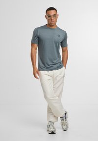 Grå kortærmet t-shirt med et logo, parret med lyse flødefarvede bukser og grå sneakers. Glat tekstur, afslappet pasform og klassisk design.