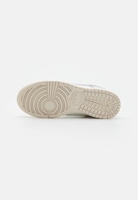 Nike sneaker bottom, featuring a textured rubber sole in beige with circular and linear patterns for grip and support.
