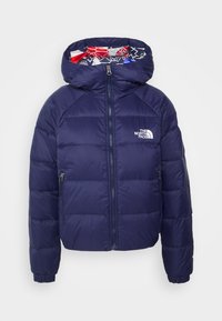 Veste matelassée bleu marine avec fermeture éclair sur le devant, poignets élastiques, capuche doublée de tissu à motifs rouge, blanc et bleu, et logo The North Face.