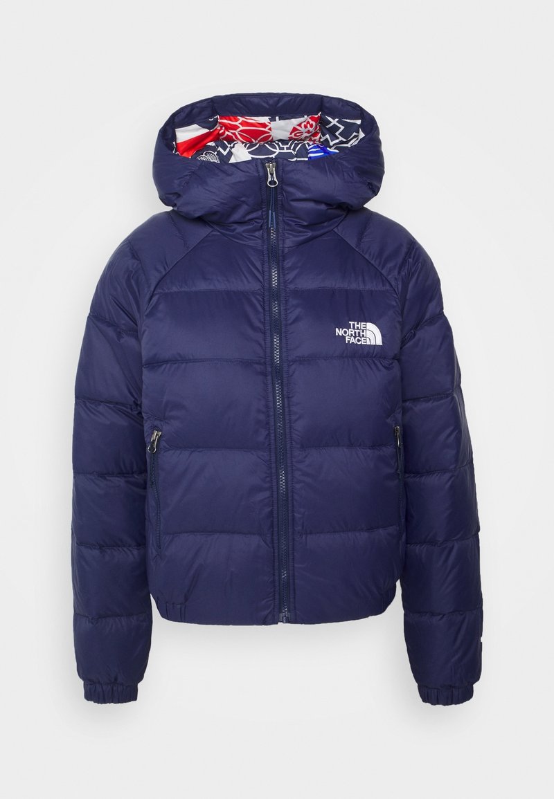 Veste matelassée bleu marine avec fermeture éclair sur le devant, poignets élastiques, capuche doublée de tissu à motifs rouge, blanc et bleu, et logo The North Face.