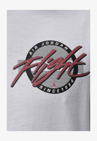 Logotipo Air Jordan Flight con letras rojas sobre un círculo negro y franjas, texto "Desde 1984" sobre fondo de tela blanca.