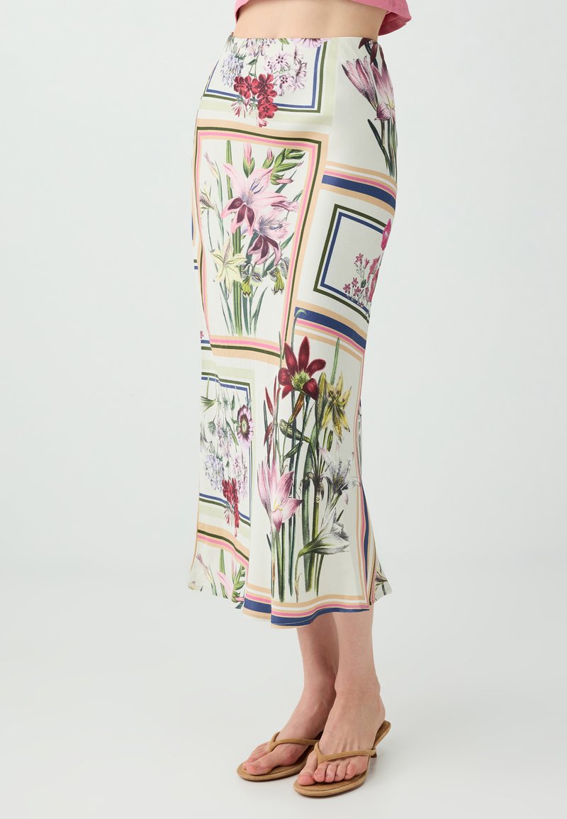Femme portant une jupe midi blanche taille haute avec des motifs carrés floraux et rayés colorés, associée à des sandales couleur cuir clair.