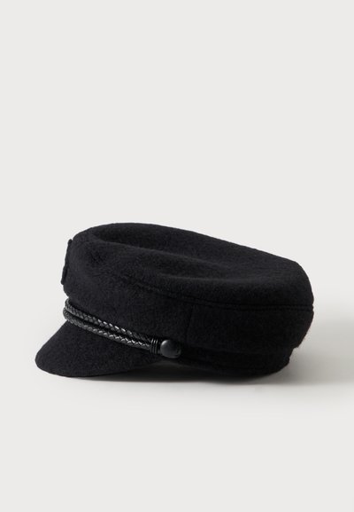 Casquette de pêcheur en laine noire avec petite visière et bande tressée décorative au-dessus de la visière, vue de côté sur fond blanc.