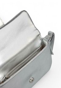 Bolso de mano metálico plateado con una textura suave, que presenta un bolsillo con cremallera y cierre a presión. El interior también es plateado y tiene un diseño elegante.