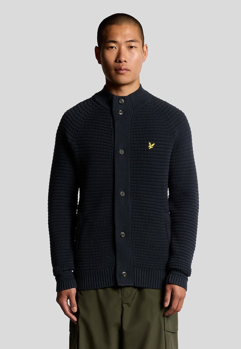 Cardigan navy lavorato a maglia con colletto alto, cinque bottoni e polsini a coste. Presenta un piccolo logo giallo sul petto sinistro.