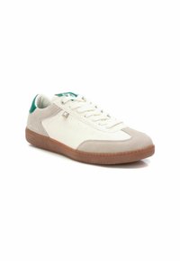 Zapatilla con parte superior de cuero blanco, acentos de gamuza beige, etiqueta de talón verde y una suela de goma texturizada color goma. Presenta cordones blancos planos.