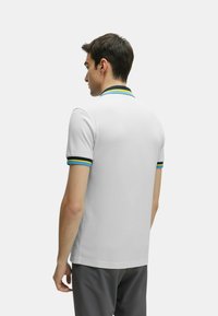Polo shirt bianco a maniche corte con colletto a coste caratterizzato da righe blu e gialle. Tessuto liscio, design aderente, orlo standard.