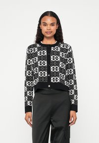 Melnā un baltā krāsā apgriezta kardigāna veste ar sarežģītiem �ģeometriskiem rakstiem, apaļu kakla izgriezumu, pogu aizdari un garām piedurknēm.