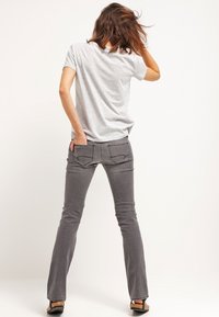 Jeans grigi flared con tasche posteriori e una maglietta grigia chiara. Il tessuto sembra morbido e leggermente strutturato. Le scarpe sono sandali neri.