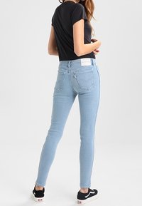 Jeans ajustados de color azul claro con una cintura de altura media, bolsillos traseros minimalistas y una etiqueta blanca de la marca en la cinturilla. Combinados con zapatillas negras.