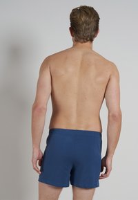 Shorts de bain bleu marine avec taille élastique, design uni, longueur mi-cuisse et texture de tissu douce, présentés de l'arrière.