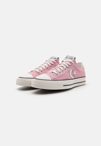 Rosa canvas sneakers med vit gummikappa, kontrasterande svarta ränder och en silverstjärna-logotyp på sidan. Snördesign, platt sula.