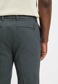 Gray herringbone trousers with a slim fit, featuring two back pockets and a smooth waistband. The fabric texture is slightly textured.