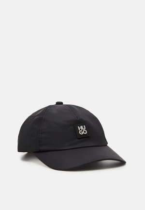 Zwarte baseballpet met gebogen klep en gestikte panelen, met een klein vierkant patch met het "HUGO"-logo aan de voorkant links.