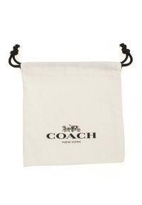 Sacoche en toile blanche avec cordon de serrage, arborant le texte noir "COACH NEW YORK" accompagné d'un motif de cheval et de carrosse. Tissu texturé avec des cordons contrastants.