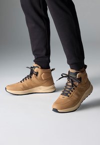 Hnědé vysoké tenisky vyrobené z membránového a syntetického materiálu, s černými tkaničkami, strukturovanými bočními panely a polstrovanou podešví.