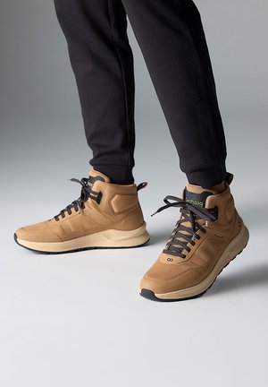 Wysokie sneakersy w kolorze brązowym, wykonane z siateczki i materiału syntetycznego, z czarnymi sznurówkami, teksturowanymi bocznymi panelami oraz amortyzowaną podeszwą.