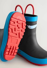 Bottes de pluie noires en caoutchouc avec des semelles texturées rouges, des accents bleus et des poignées rouges. Présentent une semelle extérieure à motifs pour une meilleure adhérence.