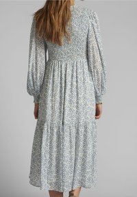 Wietrzna sukienka w kwiaty z marszczonym gorsetem, długimi bufkami i falbaniastą spódnicą, wykonana z lekkiego materiału w jasnoniebieskim i kremowym kolorze.