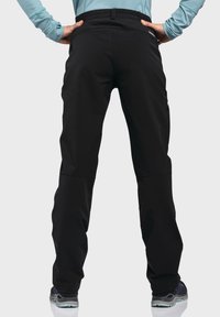 Schwarze Outdoor-Hosen mit einem flexiblen Bund, ausgestattet mit einem schmal zulaufenden Bein-Design und seitlichen Taschen, kombiniert mit dunklem Schuhwerk.