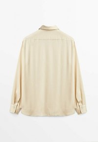 Chemise à manches longues couleur crème avec une texture lisse, un col classique et des poignets à boutons. Elle présente un dos droit et ne comporte aucun motif.