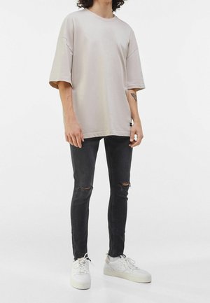Ljusbeige oversize t-shirt med nedhasade axlar, kombinerad med svarta tajta jeans med slitna knän och vita sneakers.