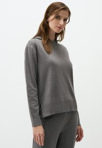 Grijze hoodie met lange mouwen, met een ontspannen pasvorm, zijsplitten en een gladde textuur. Draagt een bijpassende broek.