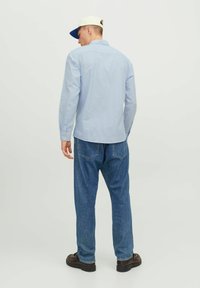 Hellblau gestreiftes Langarmhemd mit Knopfmanschetten, kombiniert mit locker sitzenden blauen Jeans und dunklen Schuhen, von hinten betrachtet.