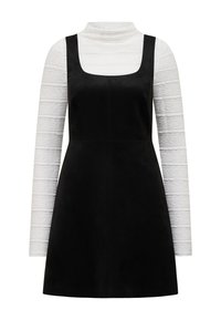 Robe noire sans manches superposée sur un haut col roulé texturé à manches longues blanc, présentée sur un fond blanc uni.