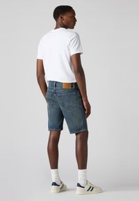 Șorturi din denim de culoare albastru estompat, cu o croială normală, dotate cu buzunare la spate, o etichetă din piele și un tiv care se termină ușor deasupra genunchiului. Tricou alb și adidași.