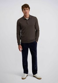 Bruine lange mouwen polo met een knoopkraag, gecombineerd met donkerblauwe corduroy broek. Witte sneakers met beige accenten. Minimalistisch ontwerp.