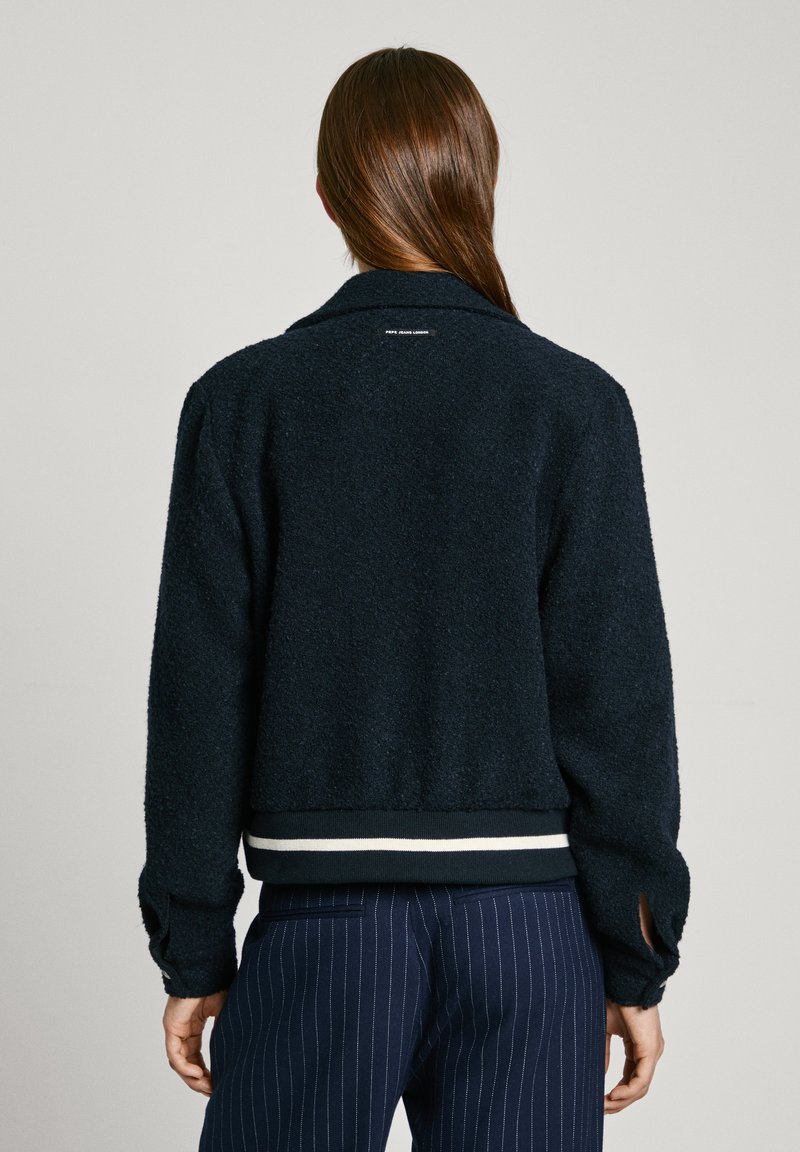 Navyblaue Fleecejacke mit weicher Textur, einem Kragen und weißen Akzentstreifen am Saum. Hat eng anliegende Ärmel und eine lässige Silhouette.