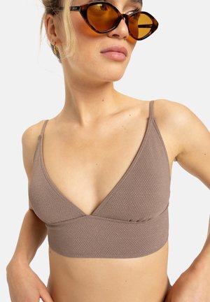 Brown textured bralette with a triangular design, featuring thin adjustable straps and a seamless band for comfort. Styled with oversized sunglasses.