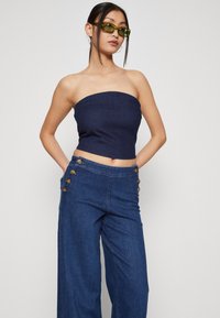 Haut sans manches en denim bleu marine associé à un pantalon en denim à jambe large avec des boutons sur les côtés. Texture lisse, design décontracté et style ajusté.