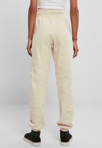 Cremfarbene Jogginghosen aus weichem Stoff, mit einem elastischen Bund und Bündchen an den Knöcheln, kombiniert mit schwarzen High-Top Sneakern.