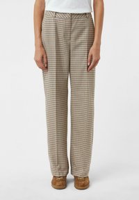 Pantaloni a quadri in tonalità beige e marroni, con una vestibilità ampia, vita alta e pieghe, realizzati in un tessuto morbido con una texture liscia.