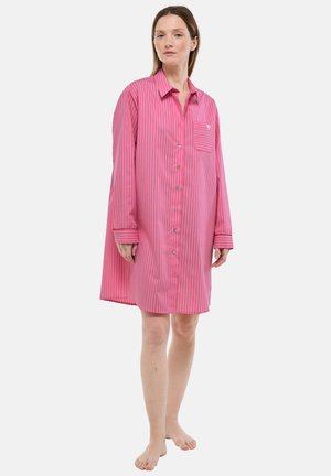 Femme debout pieds nus portant une chemise-robe ample à rayures verticales roses et blanches avec une poche poitrine.