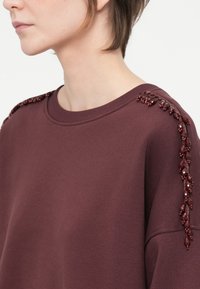 Burgundia sweatshird, mille ääre ja dekoratiivsete burgundia helmedega õlavarre õmbluse ääres. Pehme kangas ja vabalt langev lõige.