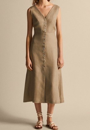 A knee-length, beige linen dress with a V-neck, sleeveless design, featuring a row of buttons down the front and a flared skirt.